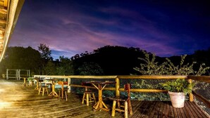 Eine Holzdar Terrasse mit Tischen, Stühlen, einem Geländer und einem Blumentopf.
