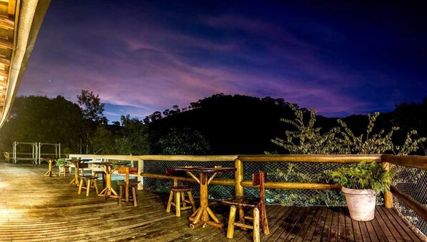 Una terraza de madera con mesas, sillas, barandilla y una maceta.