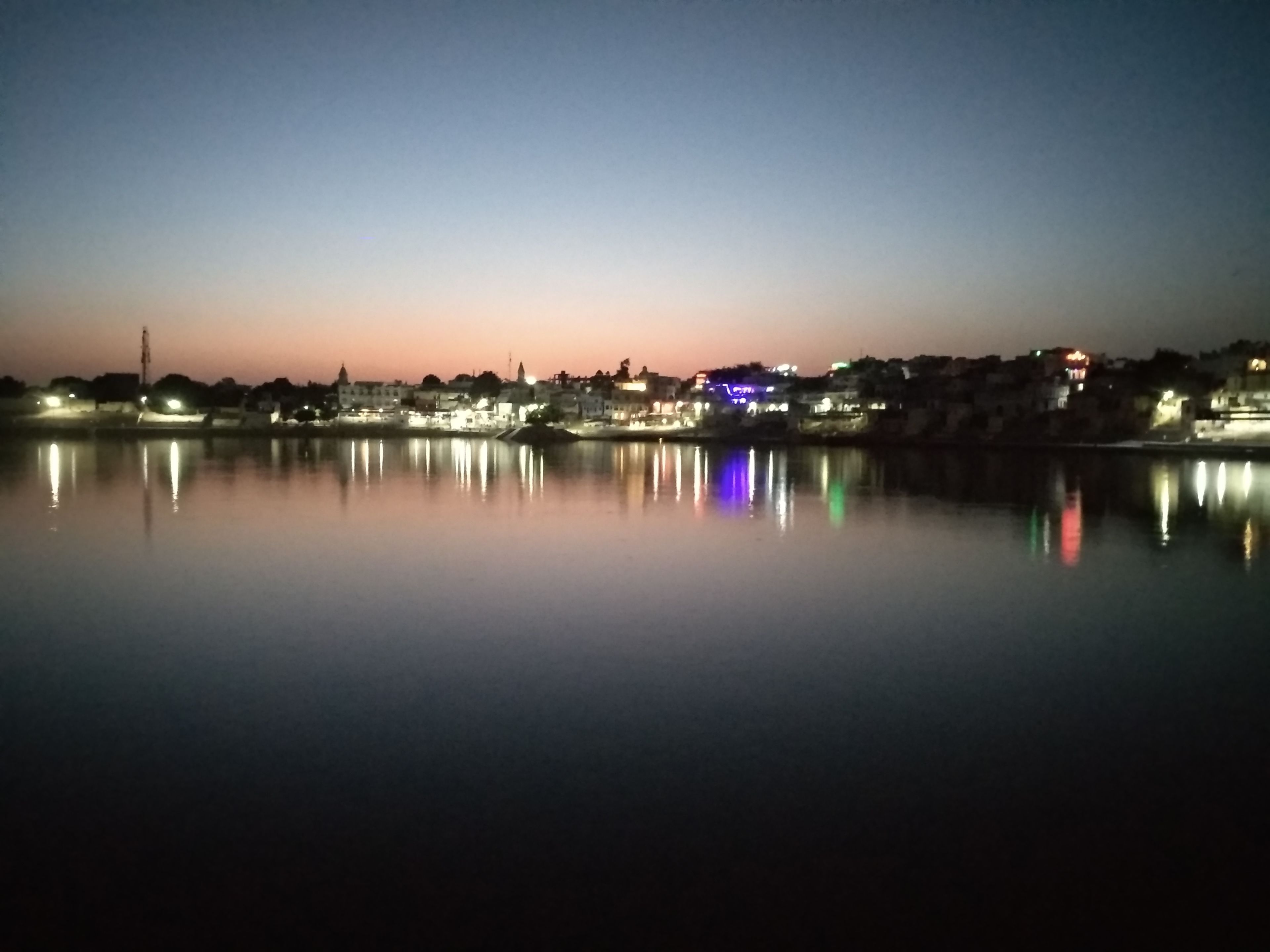 Un lago tranquilo al anochecer, con las luces de la ciudad reflejándose en el agua.