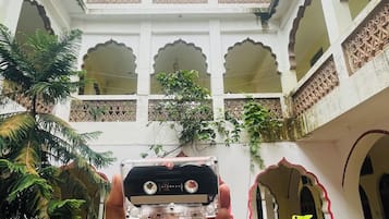 Uma mão segura uma câmera com vista para um pátio com arcos e plantas em vasos.