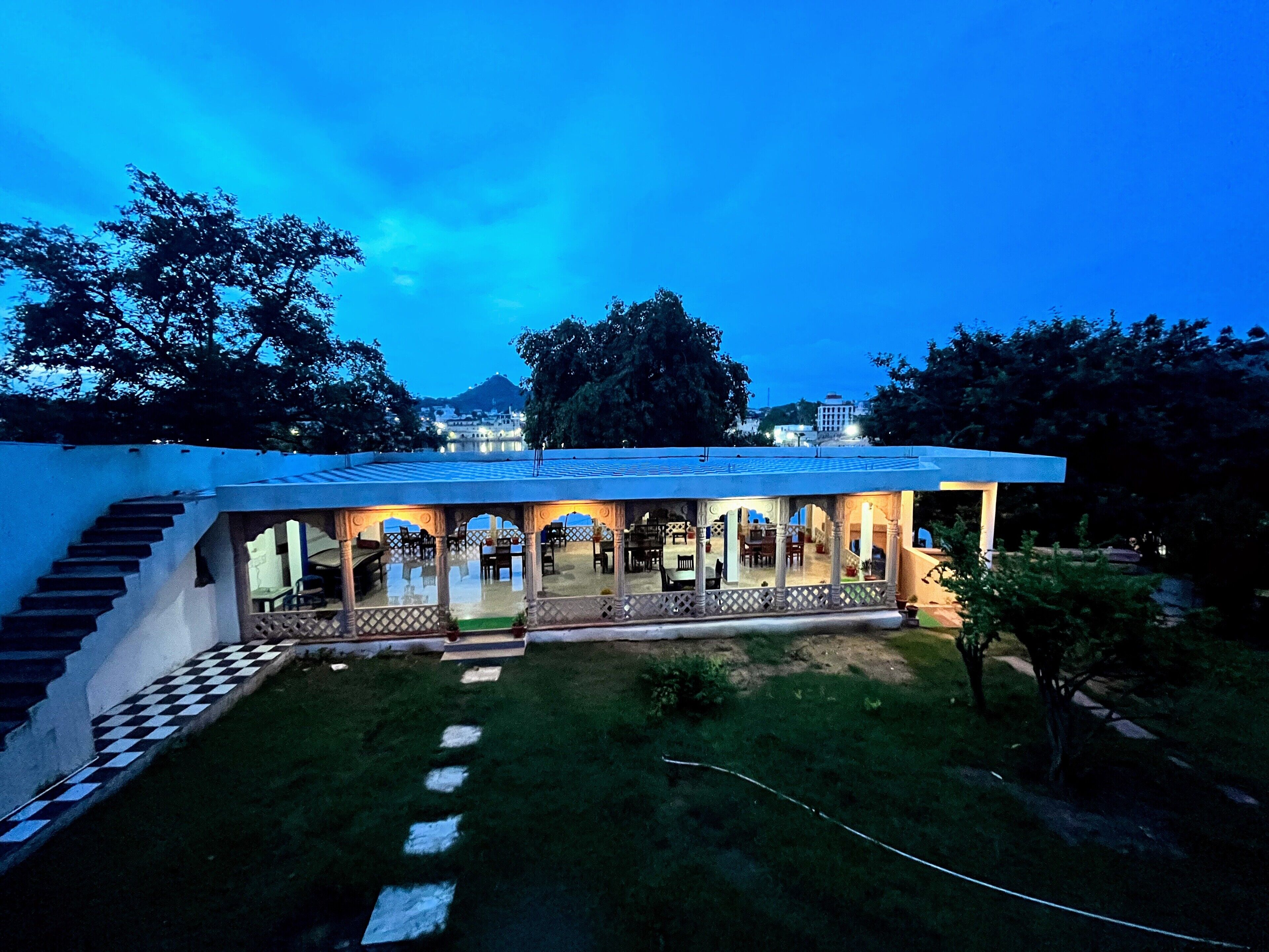 A modern building with a covered outdoor area, steps leading to the entrance, and a view of a hill in the background.