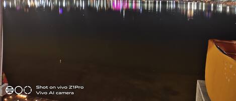 Vista nocturna de un paisaje urbano frente al agua, con edificios iluminados que se reflejan en la superficie.