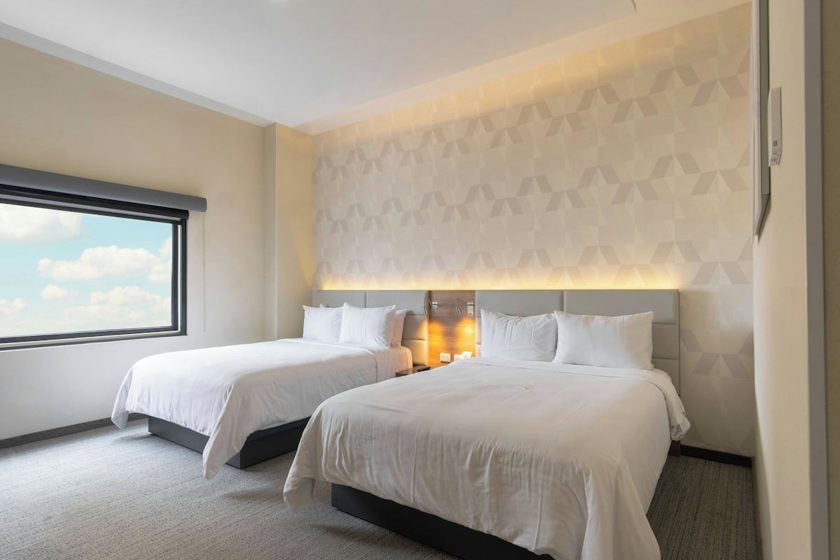 A hotel room with two beds, a large window, and a geometric patterned wall.