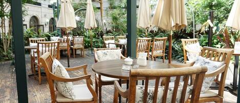 Een terras met houten tafels en stoelen, omringd door parasols en planten.