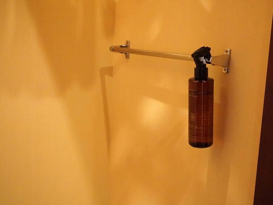 A bathroom with a yellow wall, a towel rack, and a bottle of hand sanitizer.