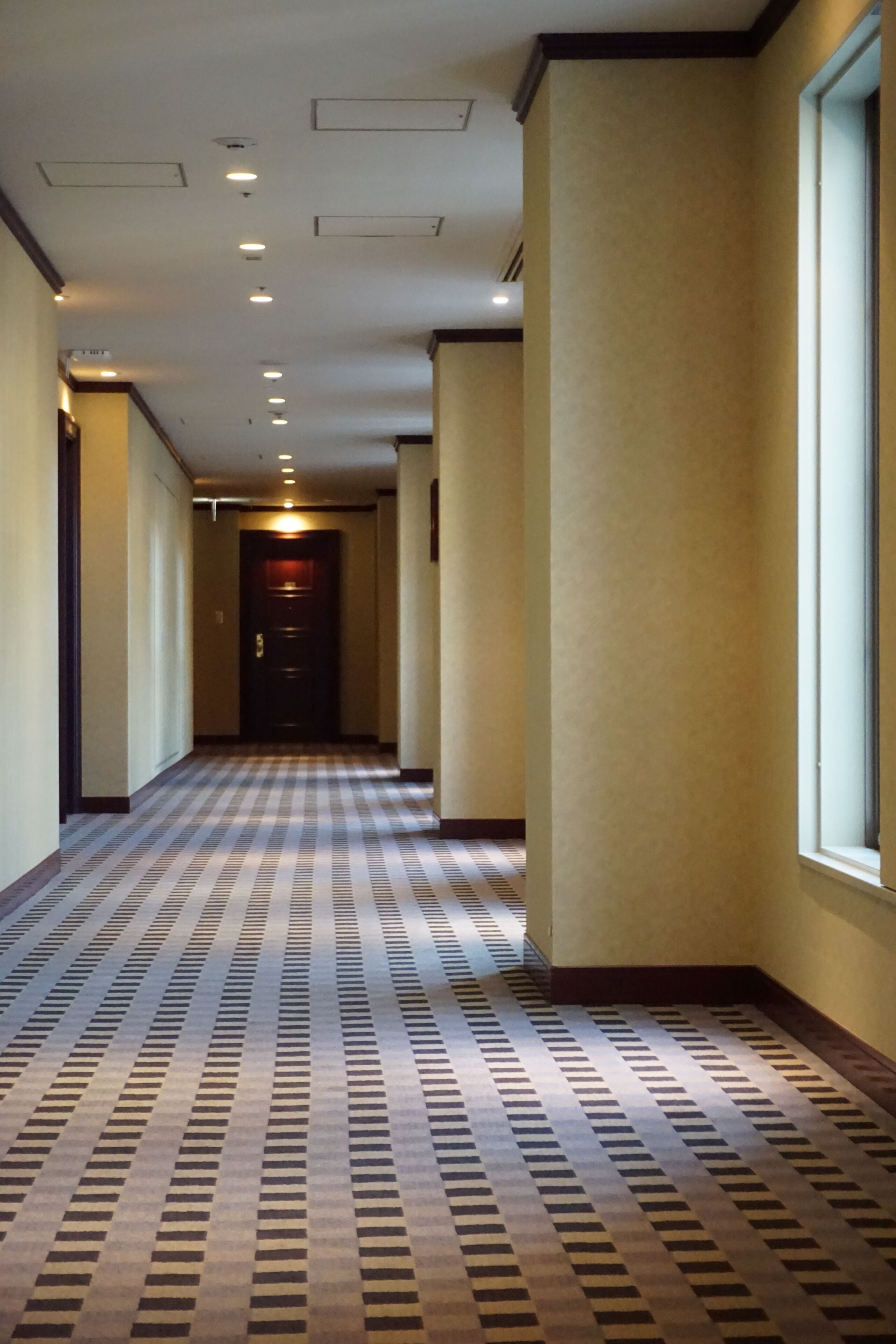 Een hotelgang met een kamerbreed tapijt, inbouwverlichting en een deur aan het einde.