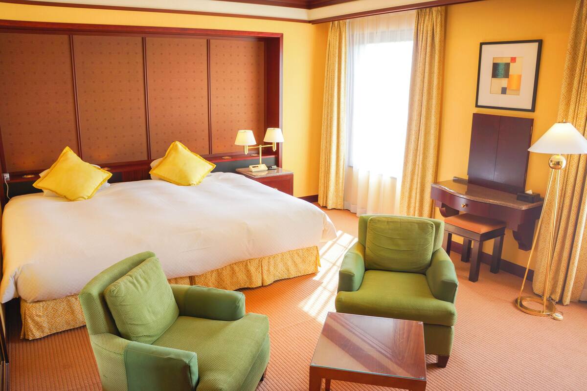 Habitación de hotel con una cama grande, dos sillones verdes, una mesita, un escritorio y una lámpara.
