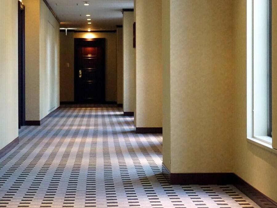 A hotel hallway with a checkered floor pattern, a door at the end, and walls with a light color.