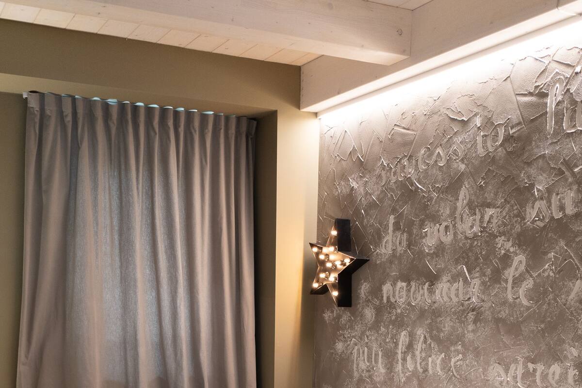 Un lit bien fait, avec du linge de lit blanc, une tête de lit en bois et un mur au motif texturé.