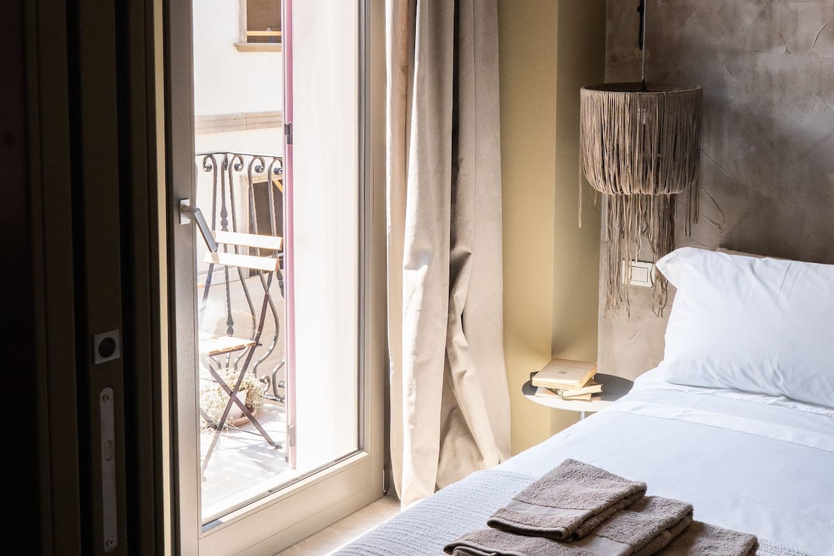 Une chambre d’hôtel avec un lit, une fenêtre avec des rideaux, un luminaire suspendu et une vue sur le balcon extérieur.