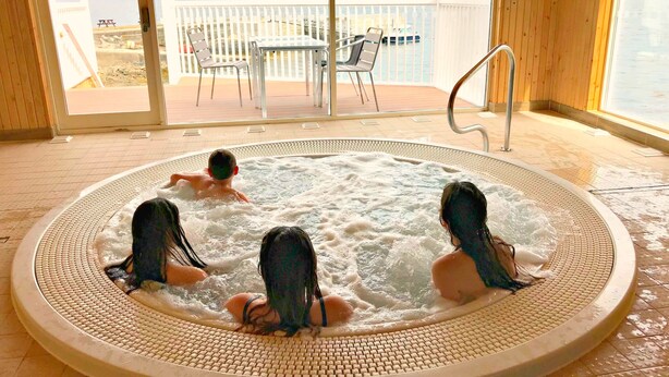 A hot tub with three people, a table and chairs outside, and a view of a lake and mountains. - Waterfront Lodges (Appin)