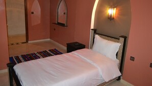 Un dormitorio con una cama, una mesita de noche, una lámpara de pared y una puerta.