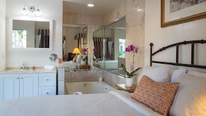 A bedroom with a large bed, a bathroom with a bathtub, a mirror, and a potted plant. - Casa Del Sol (Carpinteria)