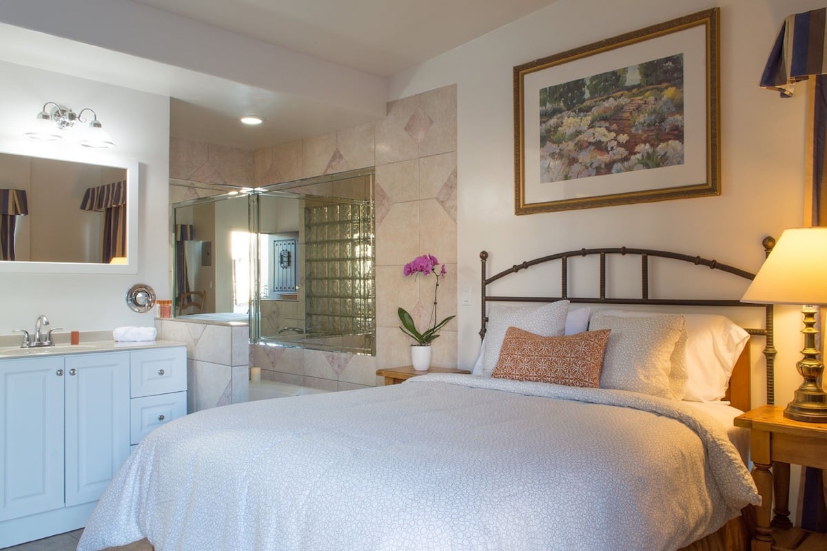 Quarto com cama, mesa de cabeceira, abajur e um espelho grande.