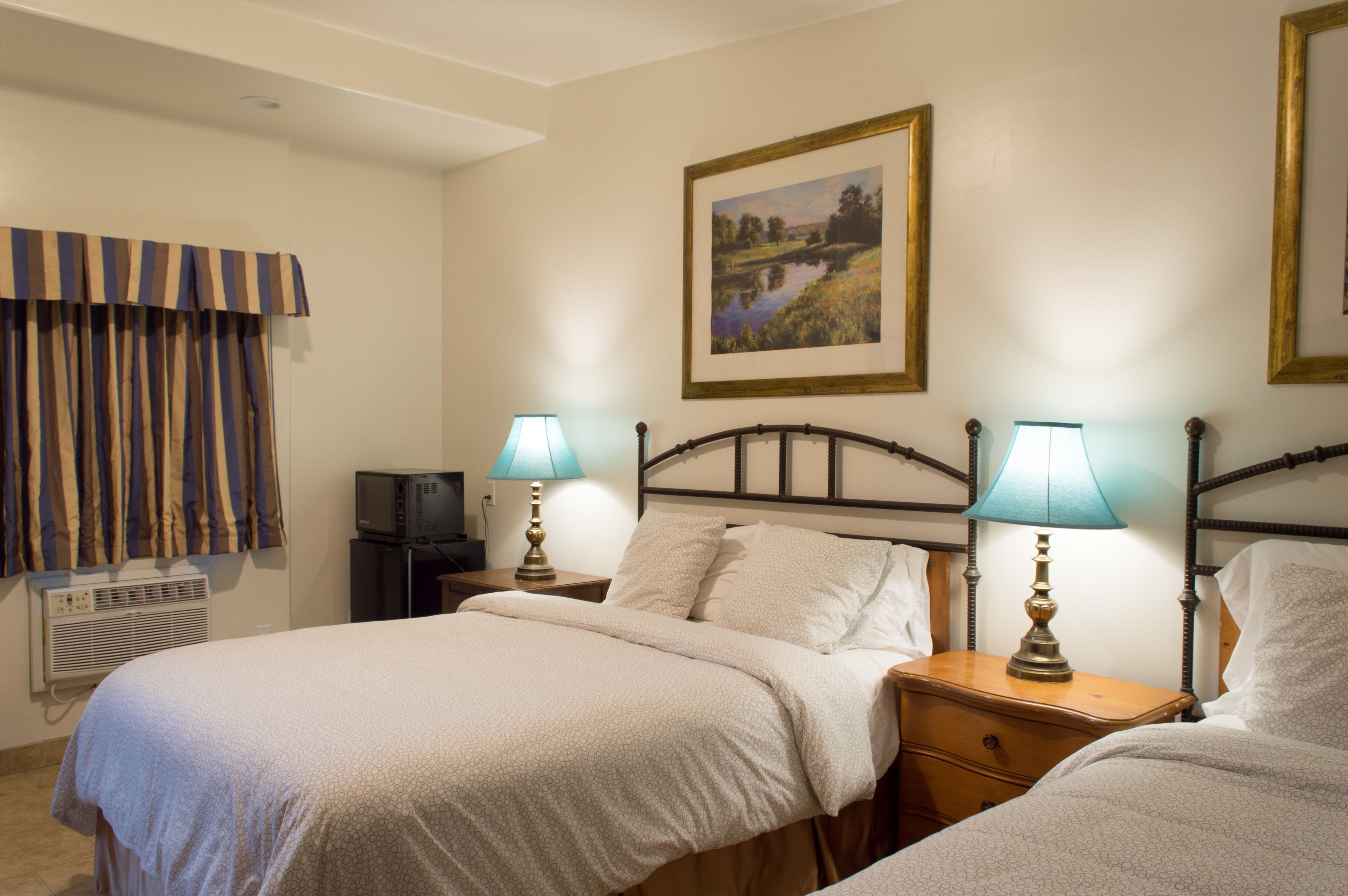 Una camera d'albergo con un letto, due comodini con lampade, un televisore, una finestra con tende e un quadro appeso al muro.