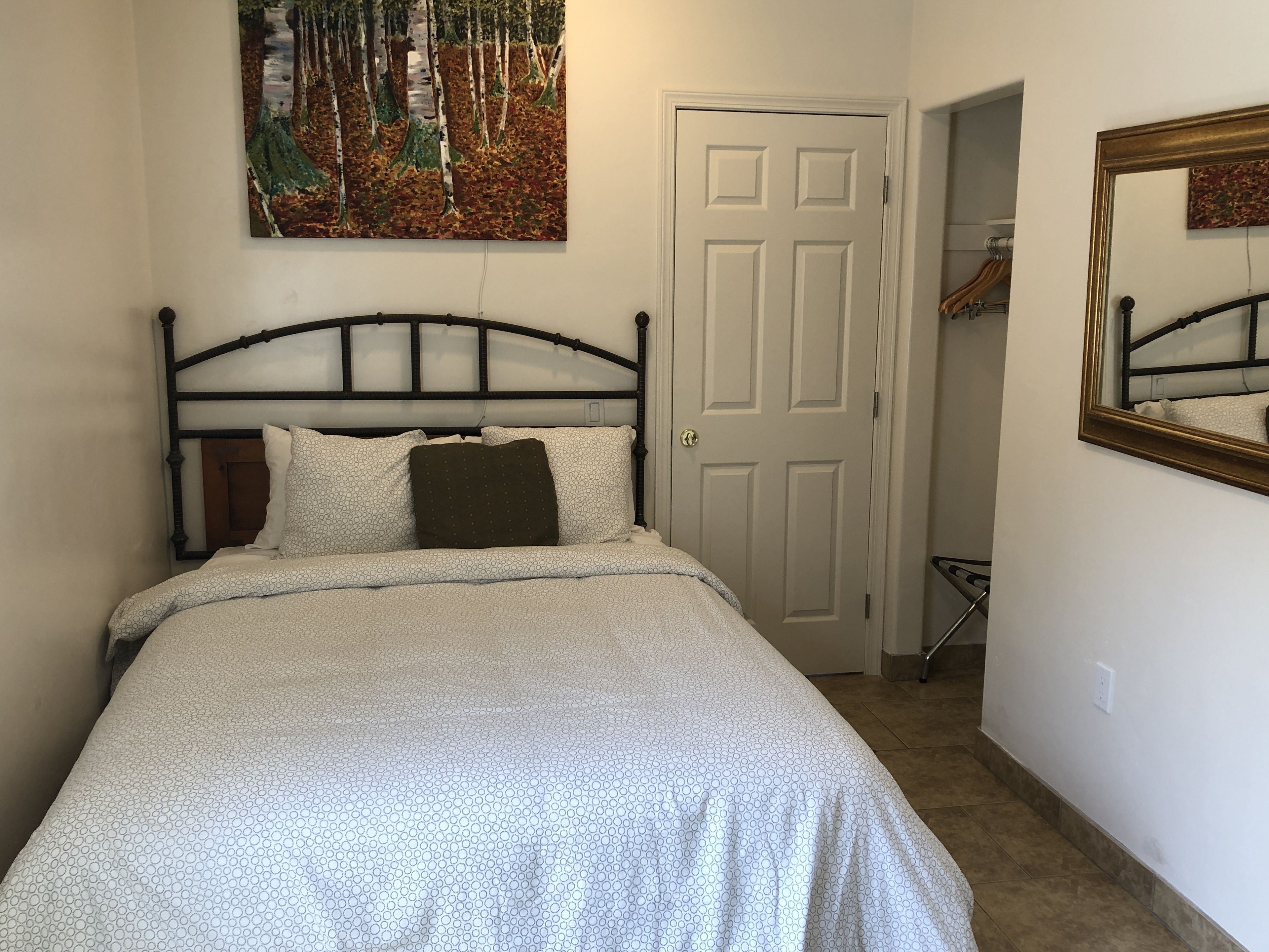 Une chambre à coucher avec un lit, une porte, un porte-manteau et un tableau accroché au mur.