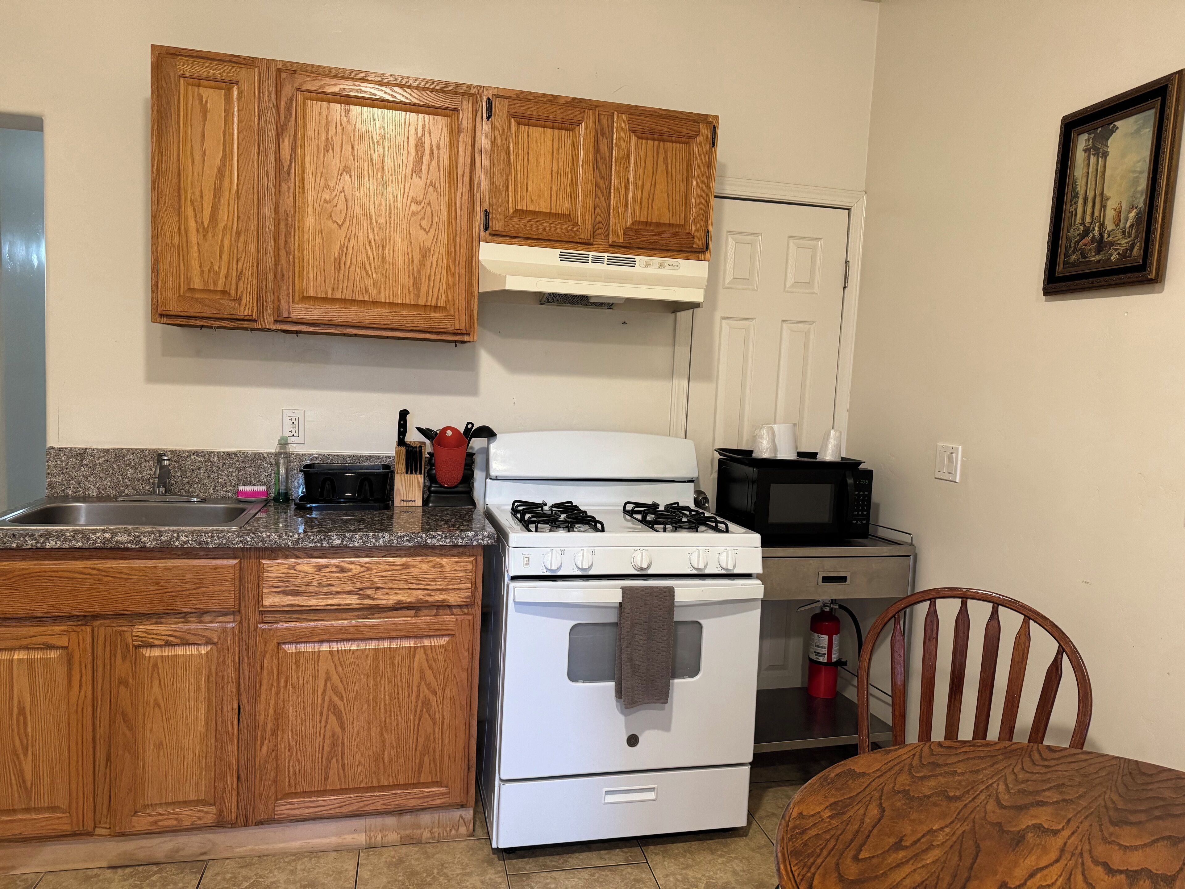A kitchen with wooden cabinets, a white stove, a microwave, and a sink.