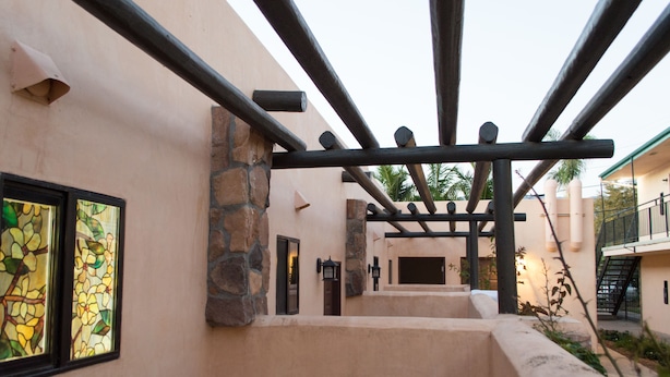A corridor with a pergola structure, stone walls, and a view of a building with a balcony. - Casa Del Sol (Carpinteria)