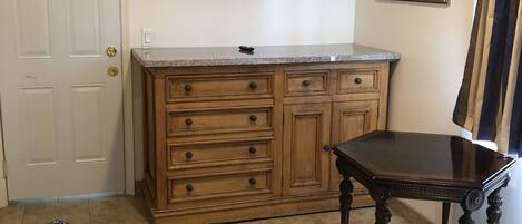Une pièce comprenant un meuble en bois, un téléviseur à écran plat fixé au-dessus, une table à manger et un lit recouvert d’une couvre-lit à motifs.