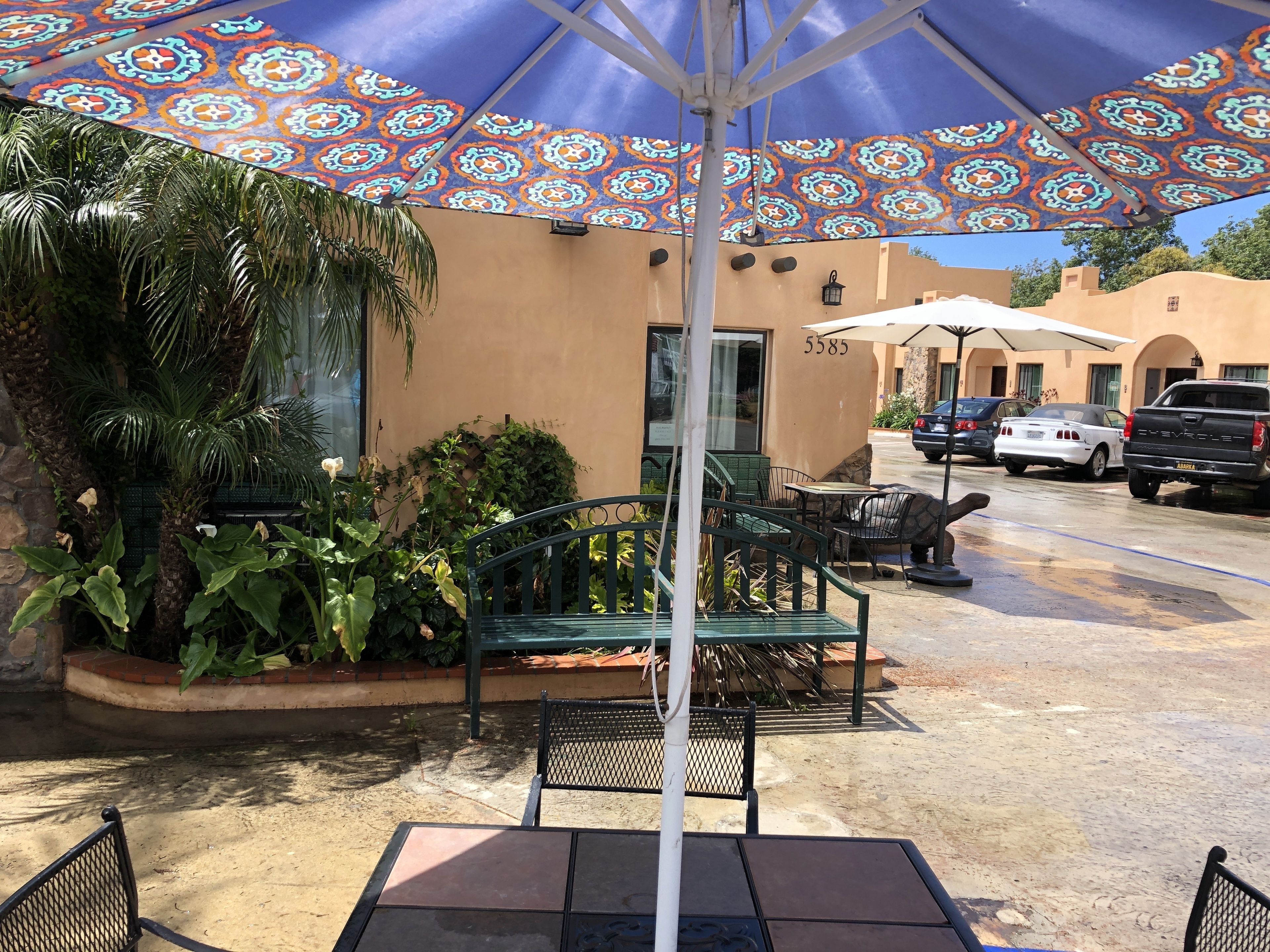 An outdoor patio with a patterned umbrella, green metal chairs, and a table.