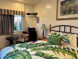 Habitación de hotel con una cama, una silla, una mesita, una lámpara, un microondas y un cuadro en la pared.