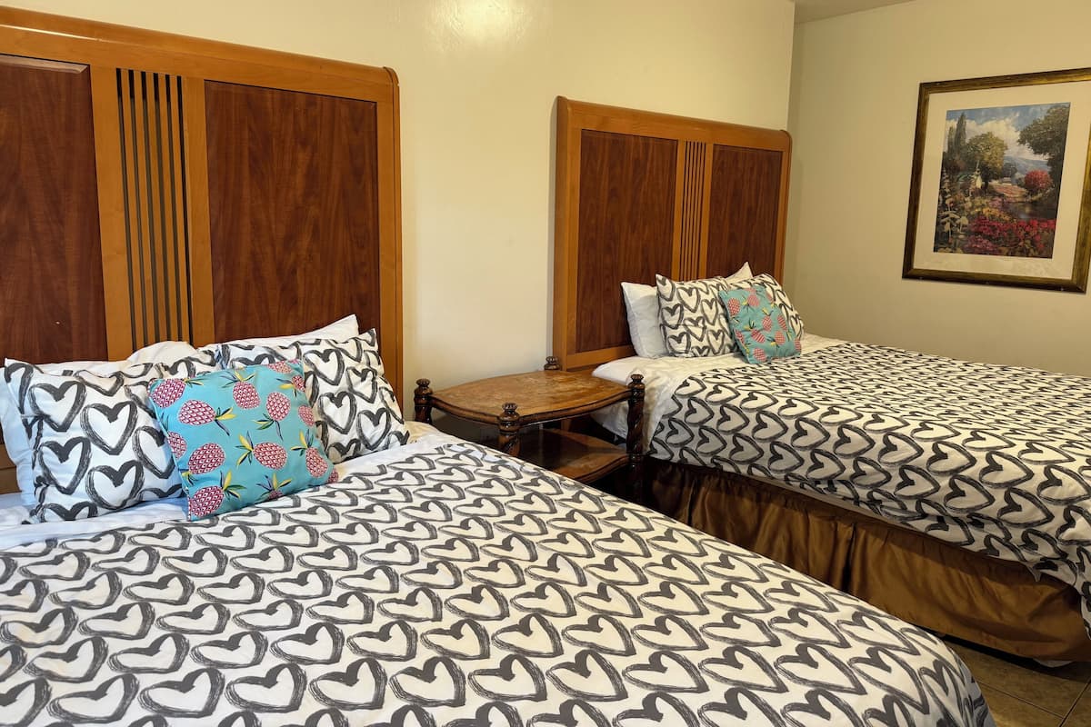 Quarto de hotel com duas camas, cada uma com colcha estampada e almofadas combinando. Cada cama tem uma cabeceira de madeira, e uma pequena mesa de cabeceira de madeira entre elas.