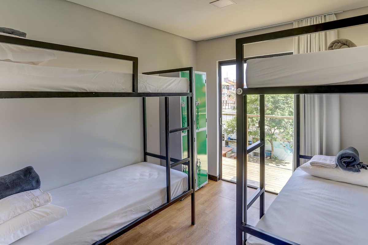 Une chambre de dortoir avec des lits superposés, une porte verte et une vue sur l’extérieur.