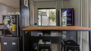 Habitación compacta con kitchenette, cafetera, refrigerador y ventana con vistas a edificios.
