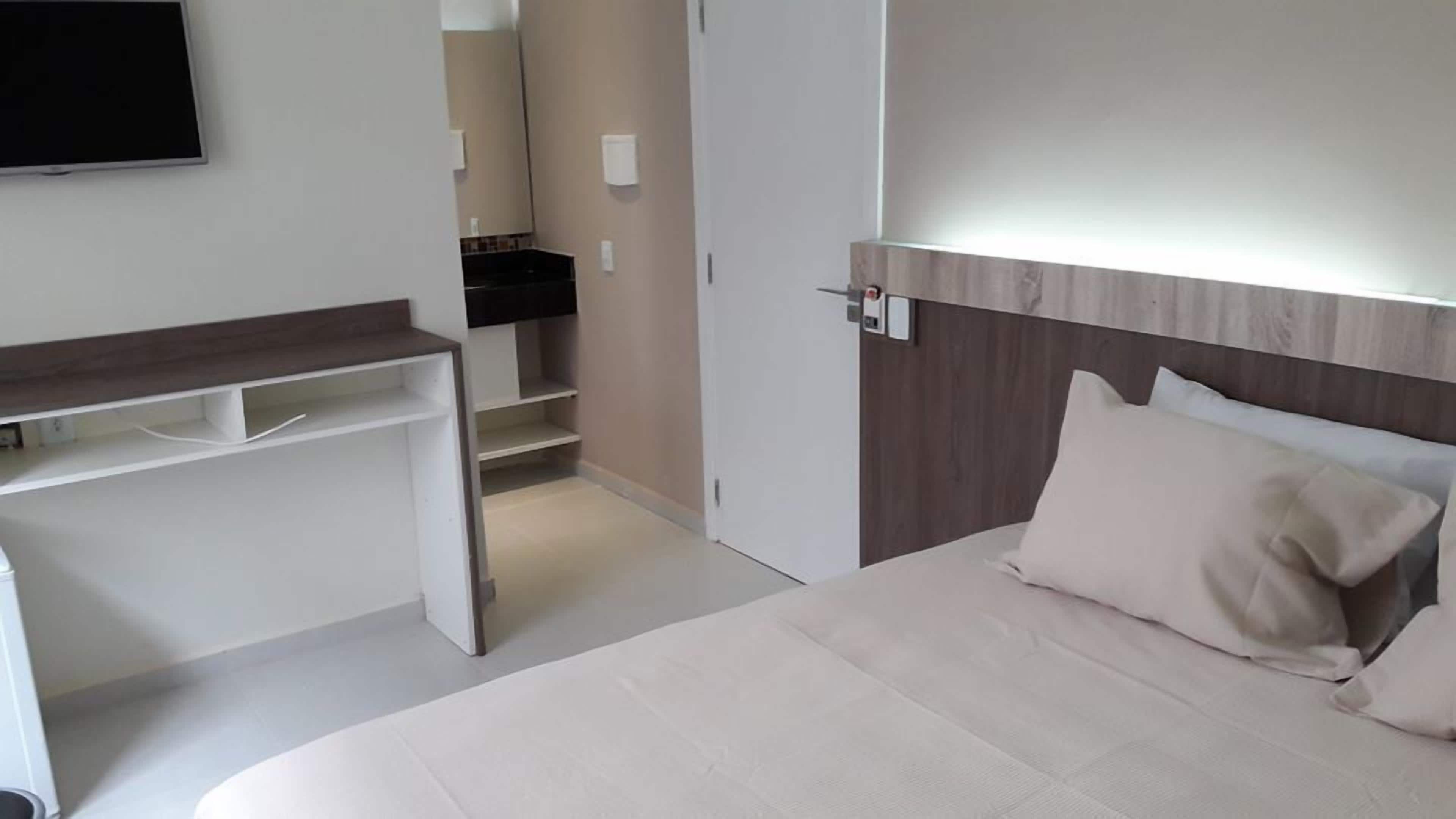 Quarto com cama, escrivaninha e espelho.