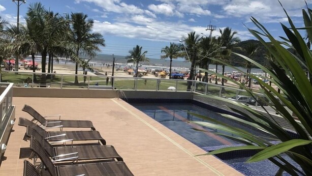 A pool area with lounge chairs, a small pool, and a view of a beach with palm trees and umbrellas. - Pousada Cantinho Oriental (Bertioga)