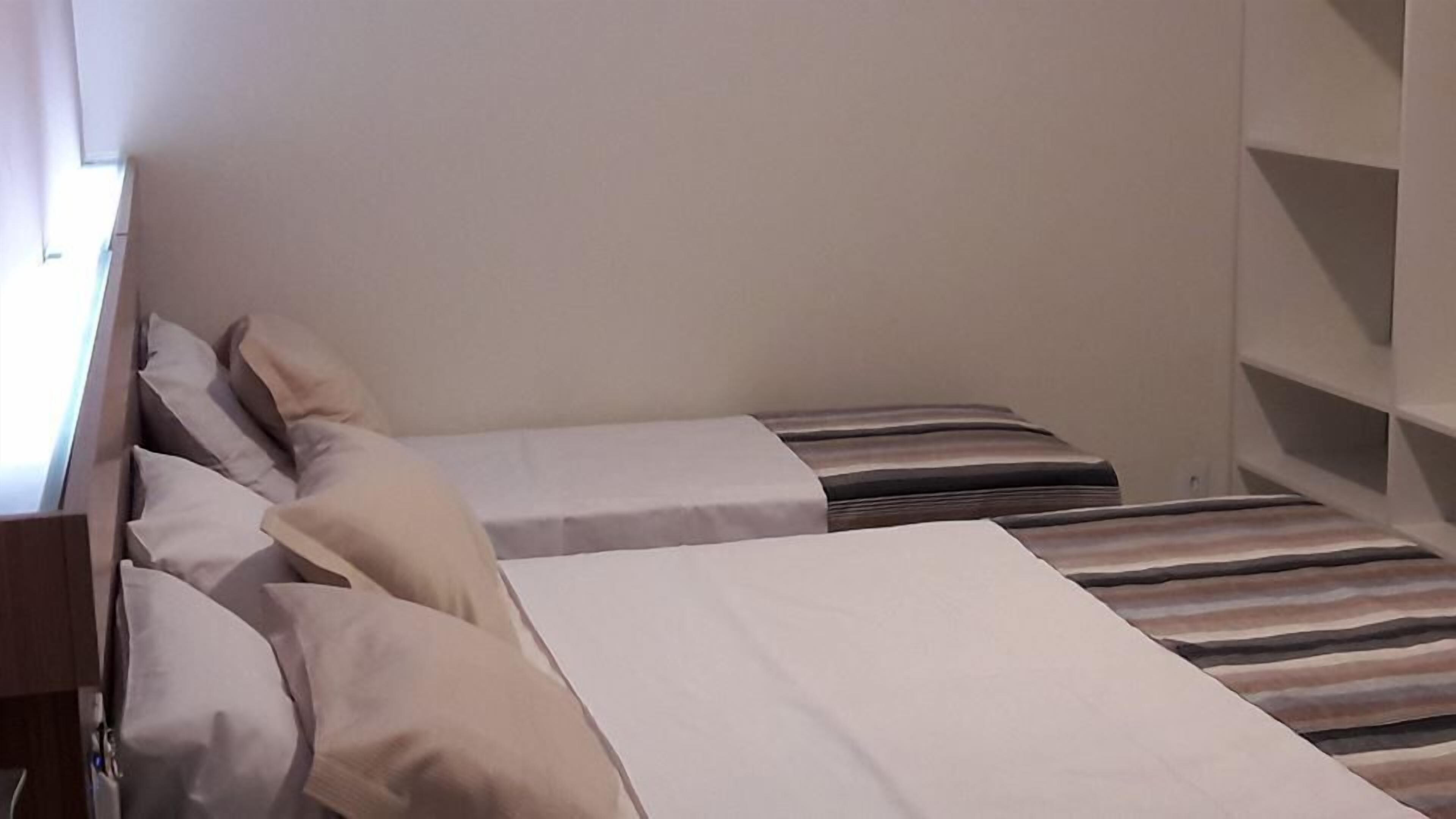 Een kleine, compacte kamer met twee eenpersoonsbedden, elk voorzien van een gestreept dekbedovertrek en meerdere kussens.