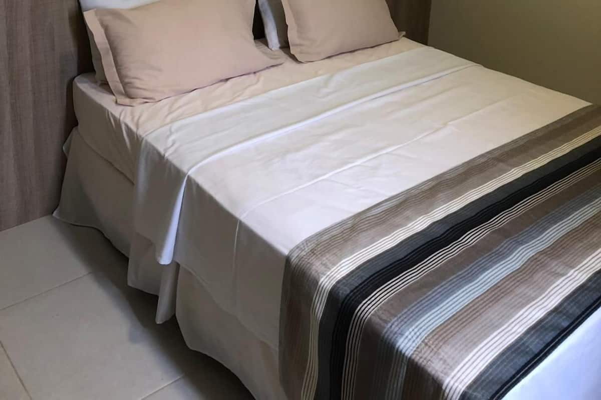 A neatly made bed with a striped blanket and two pillows, a wooden headboard, and a wall with a geometric light fixture.