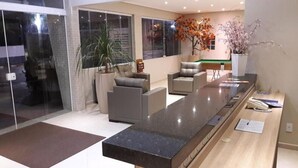 A modern reception area with a long counter, seating, and decorative plants. - Pousada Cantinho Oriental (Bertioga)