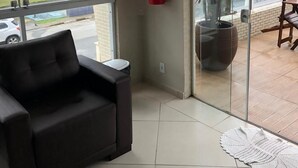 A modern room with a black sofa, a fire extinguisher, a large window with a view of the beach, and a potted plant. - Pousada Cantinho Oriental (Bertioga)