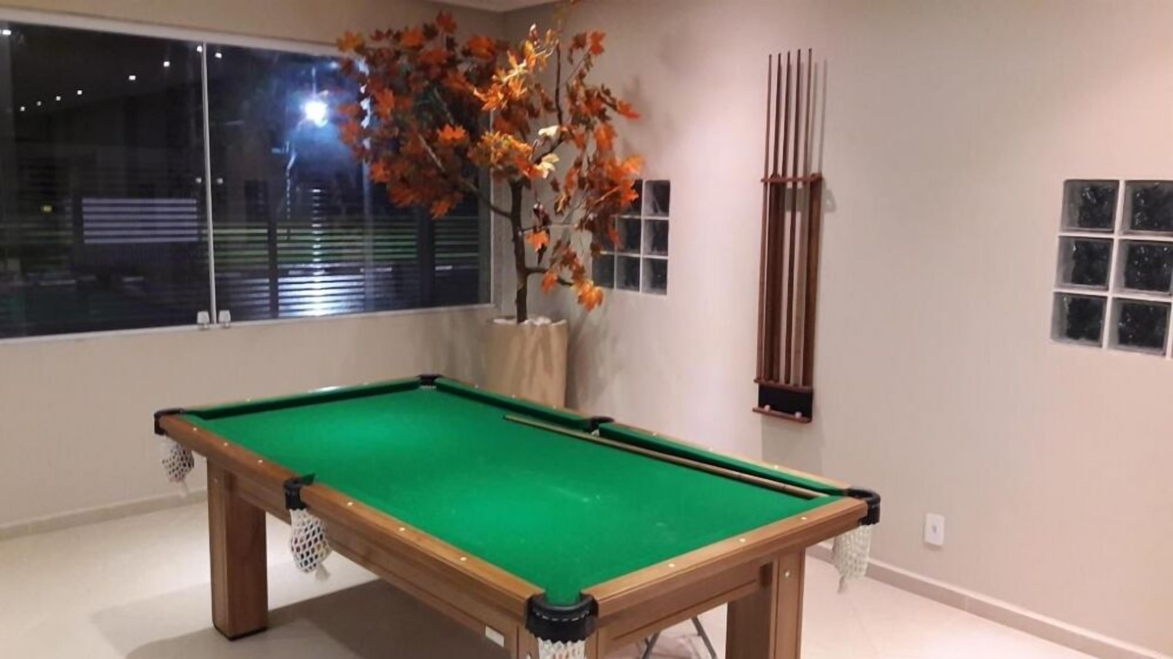 Una mesa de billar en una habitación con un ventanal grande, un jarrón con hojas otoñales y una estructura de madera vertical.