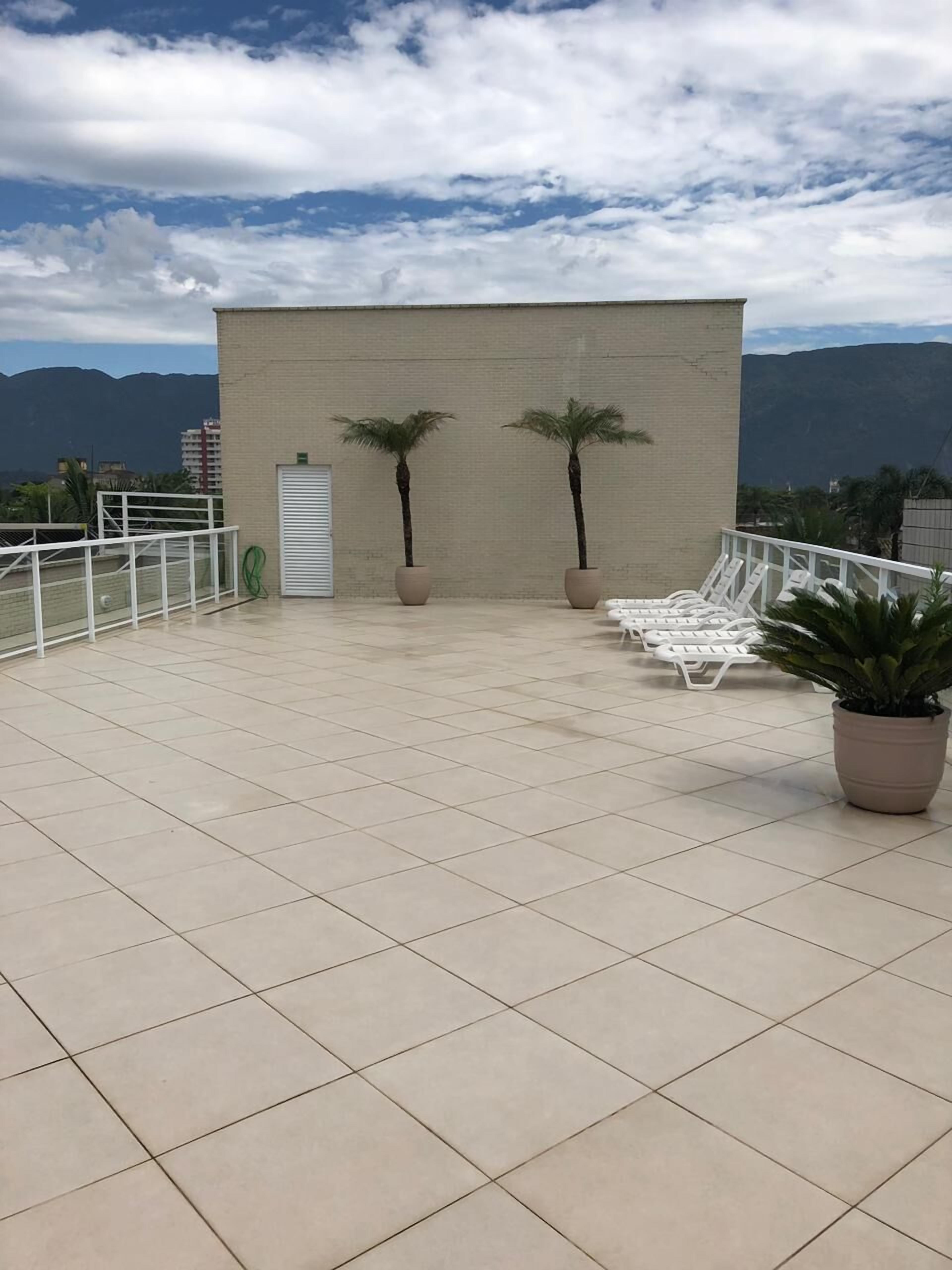 Una terraza en la azotea con suelo de baldosas, dos palmeras y sillones blancos para lounge.