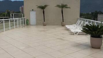 Una terraza en la azotea con suelo de baldosas, dos palmeras y sillones blancos para lounge.