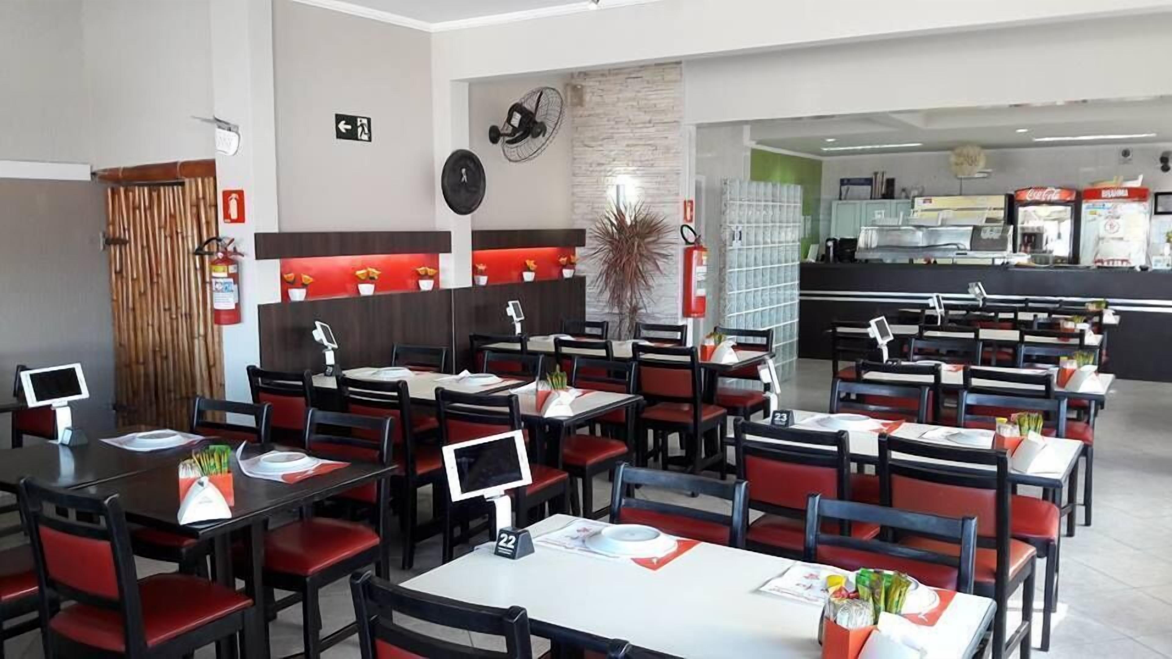 Um restaurante com várias mesas e cadeiras, uma área de balcão e um extintor de incêndio na parede.