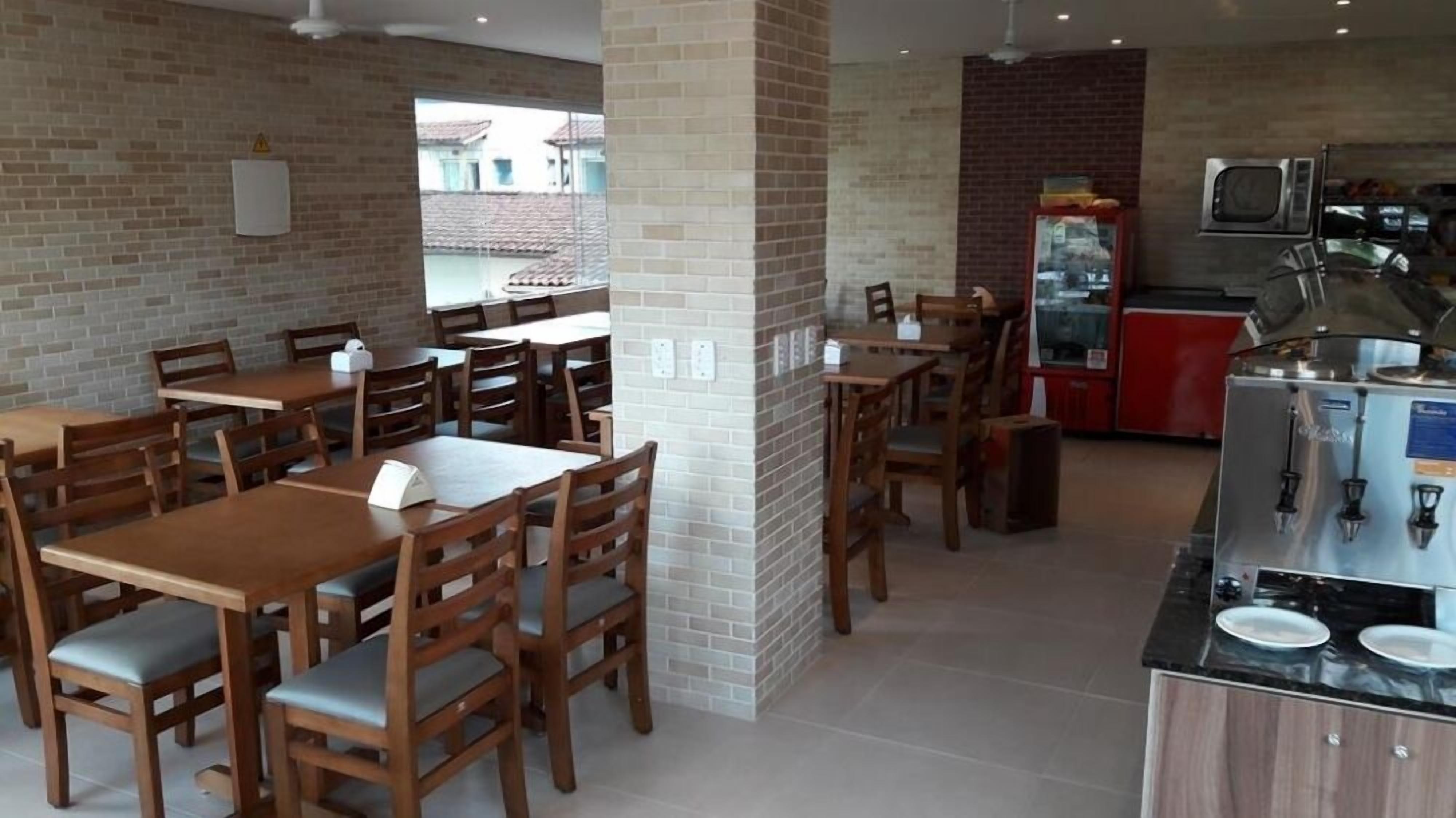 Un restaurant aux murs de briques, avec des tables et des chaises en bois, un réfrigérateur rouge et une machine à café.