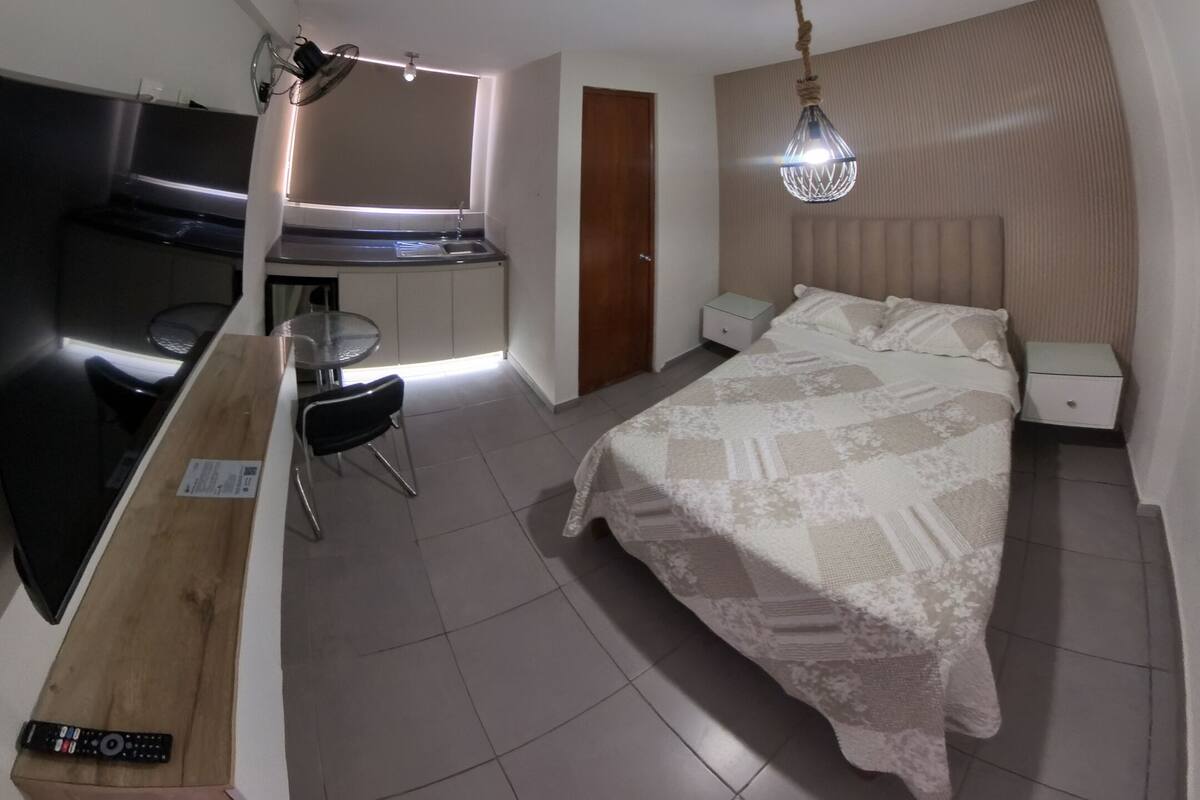 A bedroom with a bed, bedside table, nightstand, and a small window.