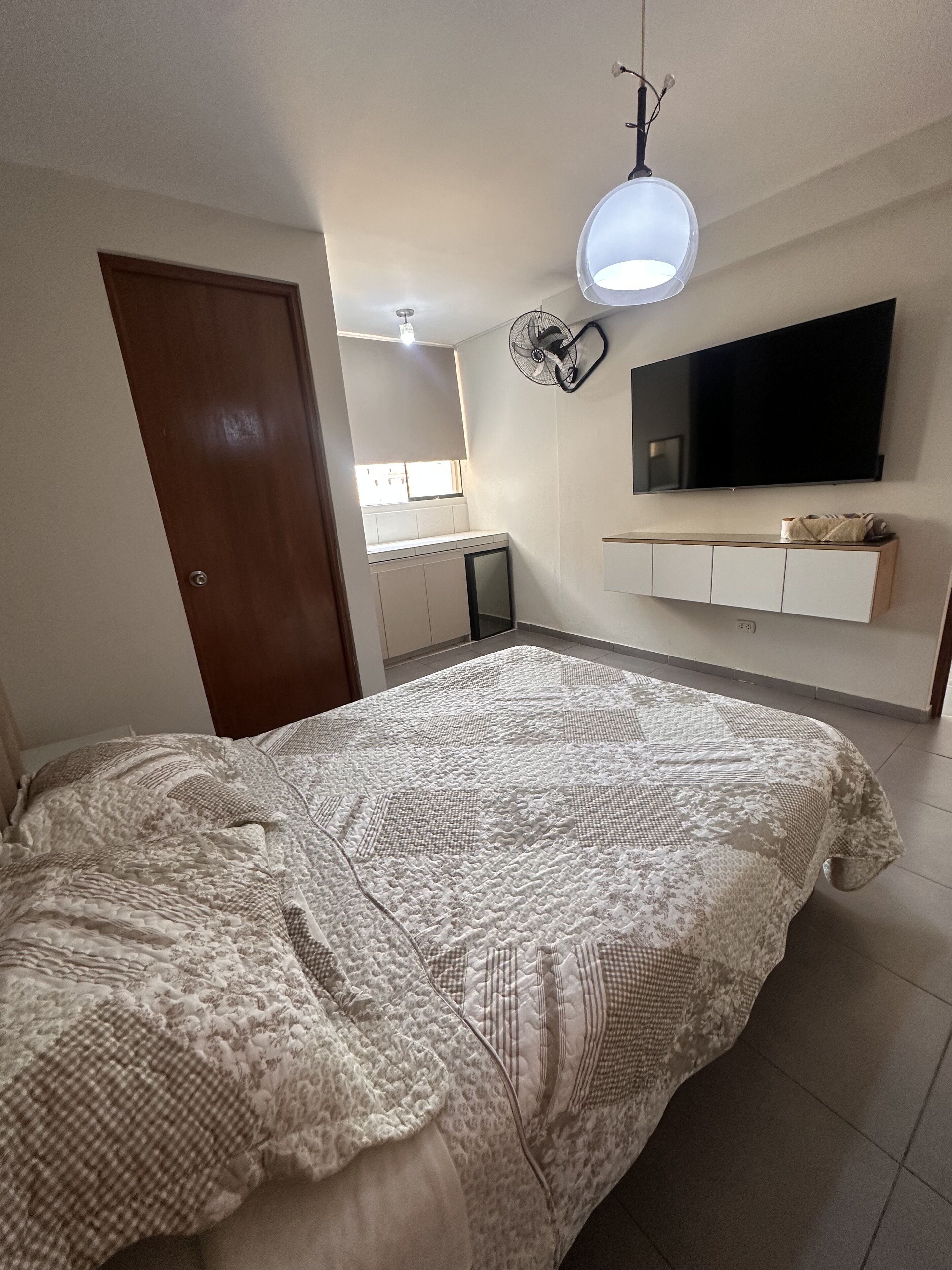 Une chambre avec un grand lit, un téléviseur fixé au mur et un ventilateur de plafond.