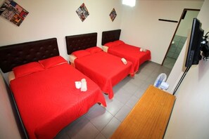 A hotel room with three beds, each with a red bedspread and a wooden headboard. There is a wooden table and a television on a stand. - G-Boss Hotel Sur (Lurín)
