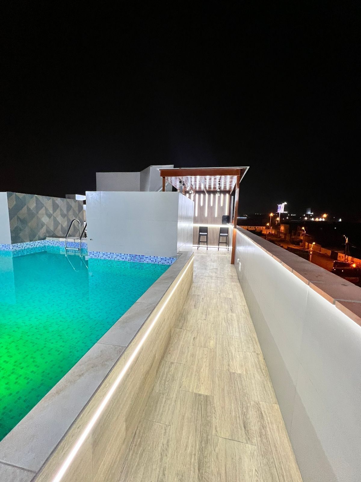 A rooftop swimming pool with a wooden deck and a covered seating area.