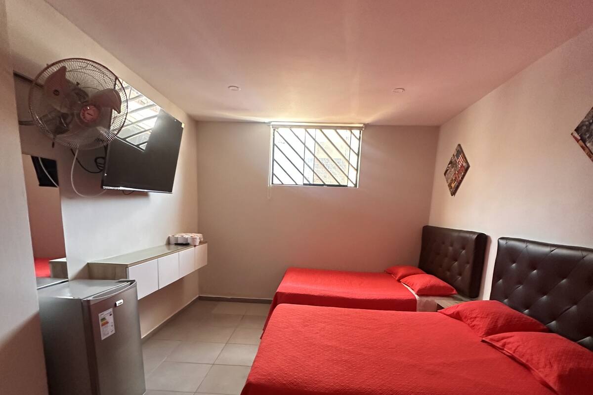 A room with two beds, a small fridge, a TV mounted on the wall, and a window with bars.