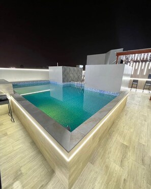 Una piscina rectangular con borde de azulejos, rodeada por un suelo de color claro y un muro bajo.