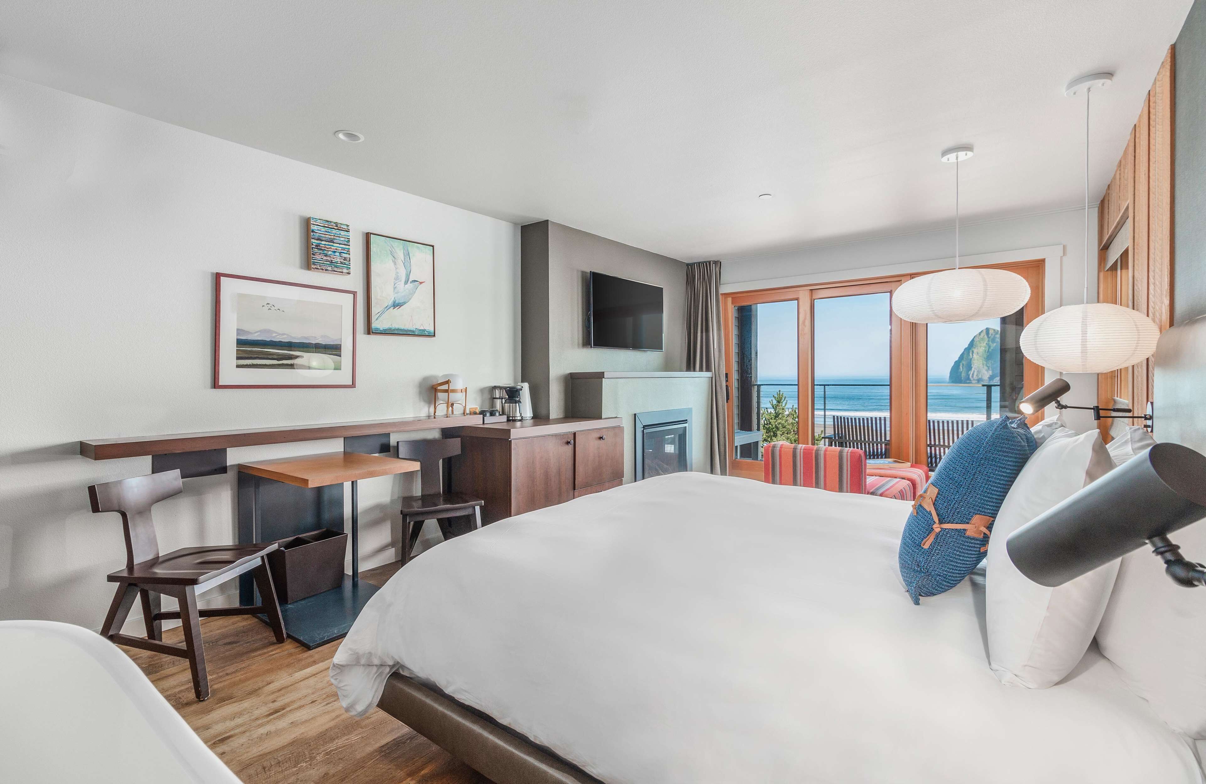 A hotel room with a bed, a desk, a chair, a TV, and a balcony with a view of the sea.
