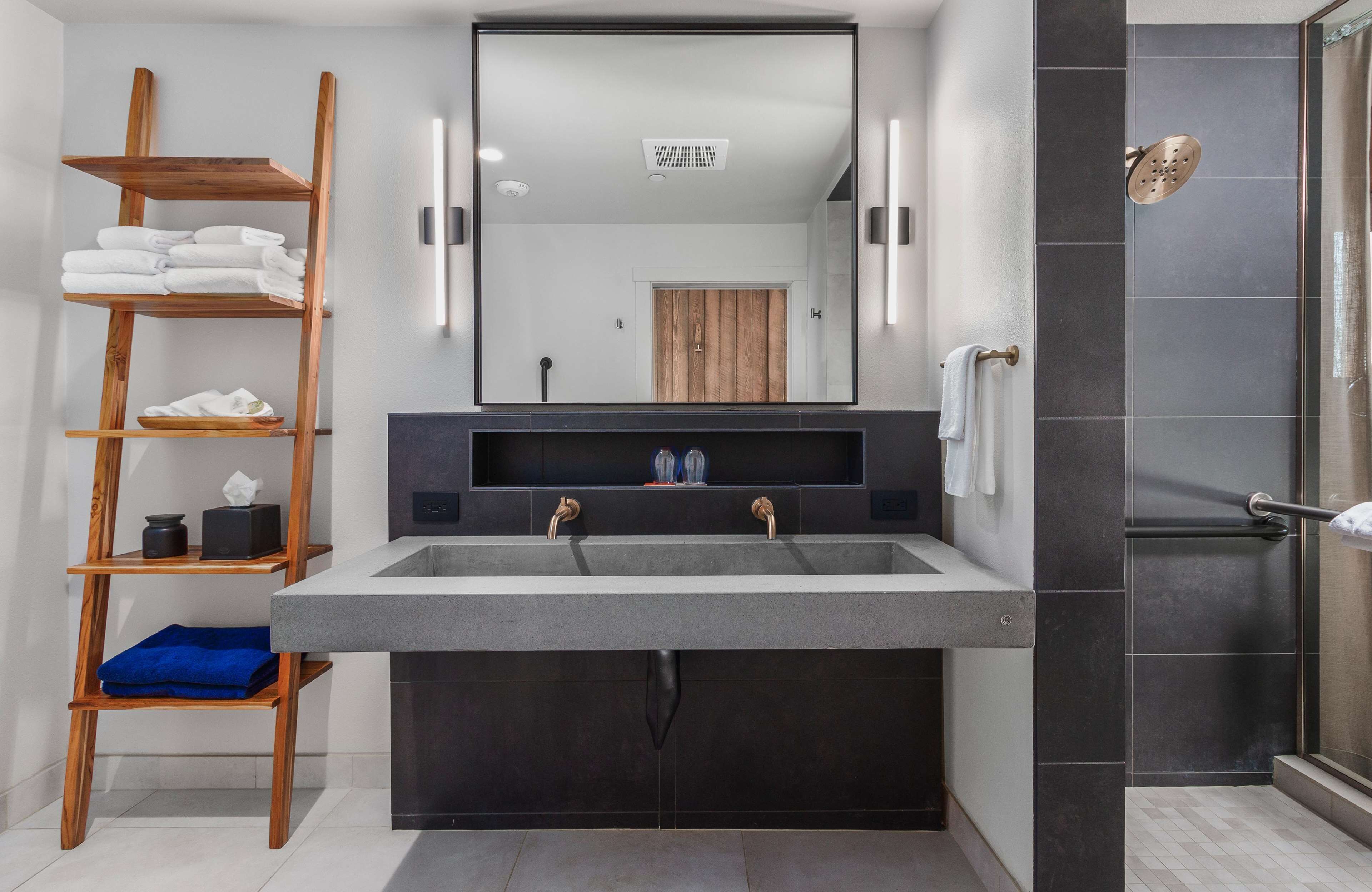 A modern bathroom with a large sink, wooden shelves, and a shower area.