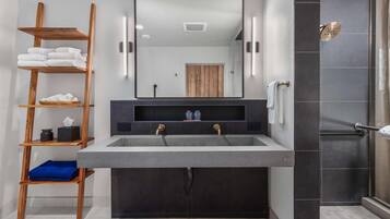A modern bathroom with a large sink, wooden shelves, and a shower area.