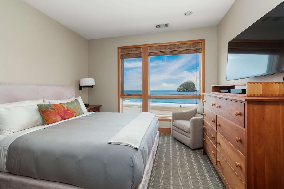 Une chambre avec un grand lit, une commode, une télévision et une fenêtre donnant sur la plage.