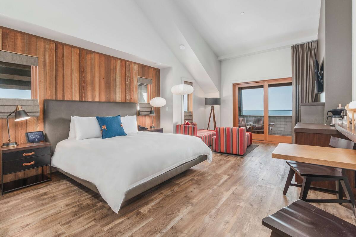 Une chambre d’hôtel moderne dotée d’un grand lit, de murs recouverts de panneaux en bois, d’un balcon avec vue et d’une kitchenette.